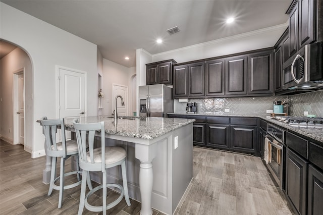 kitchen with appliances with stainless steel finishes, a center island with sink, light stone counters, and sink