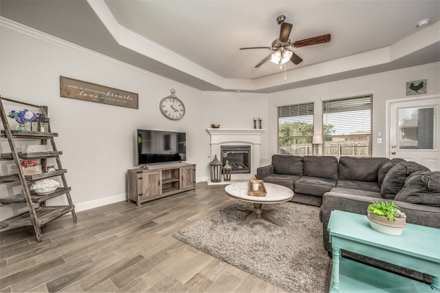 living room with a tray ceiling, hardwood / wood-style flooring, ornamental molding, and ceiling fan