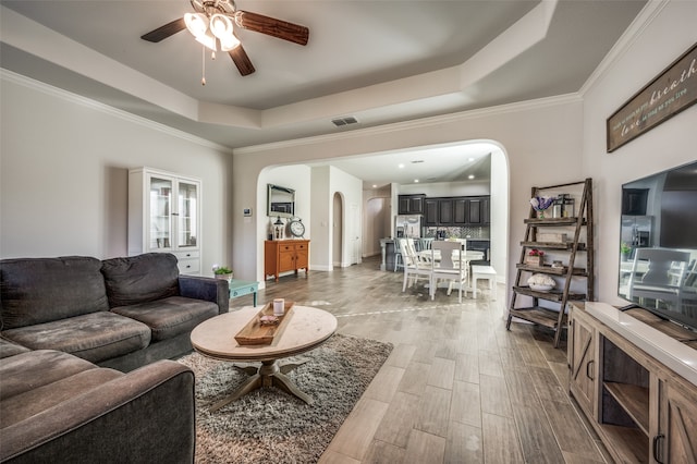 living room featuring ceiling fan, light hardwood / wood-style flooring, crown molding, and a tray ceiling