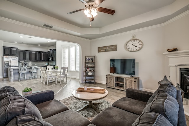 living room featuring ceiling fan, a raised ceiling, crown molding, and light hardwood / wood-style flooring