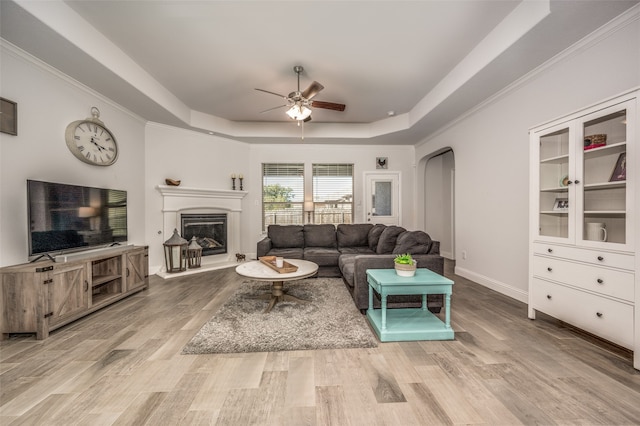 living room with ceiling fan, light wood-type flooring, and a tray ceiling