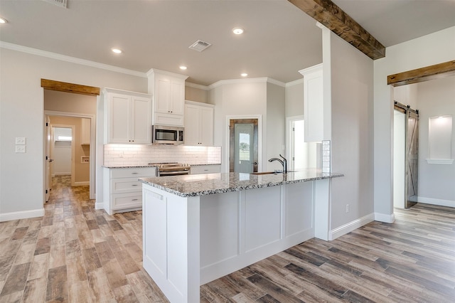 kitchen featuring a barn door, stainless steel appliances, white cabinetry, and light hardwood / wood-style flooring