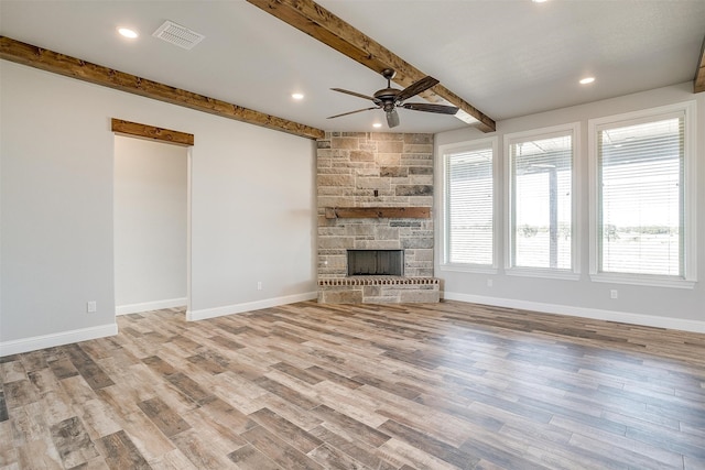 unfurnished living room featuring beam ceiling, a stone fireplace, ceiling fan, and light wood-type flooring