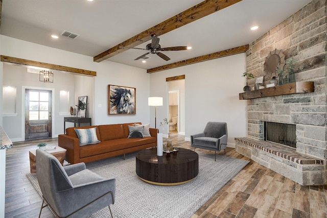 living room with a stone fireplace, ceiling fan, beamed ceiling, and wood-type flooring