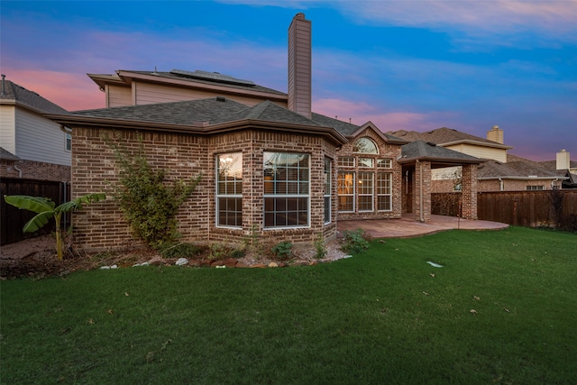 back house at dusk with a lawn and a patio