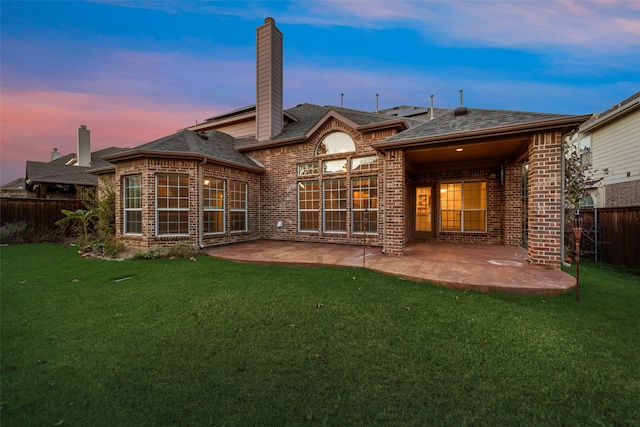 back house at dusk featuring a lawn and a patio area