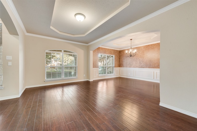 unfurnished room with dark hardwood / wood-style flooring, an inviting chandelier, a textured ceiling, ornamental molding, and a raised ceiling