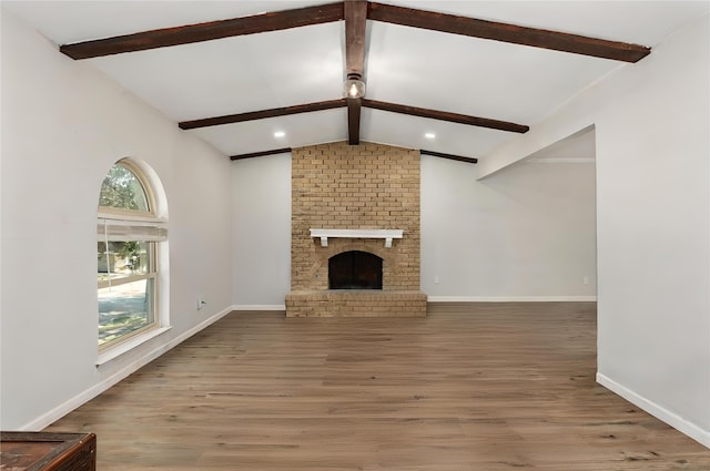 living room featuring vaulted ceiling with beams, light hardwood / wood-style flooring, a healthy amount of sunlight, and a brick fireplace