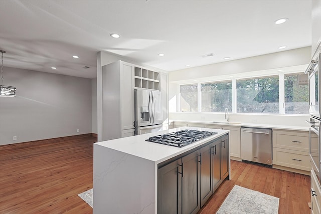 kitchen featuring white cabinetry, sink, appliances with stainless steel finishes, decorative light fixtures, and light hardwood / wood-style flooring