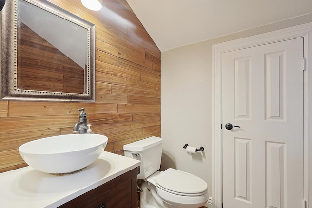 bathroom featuring toilet, vanity, lofted ceiling, and wooden walls