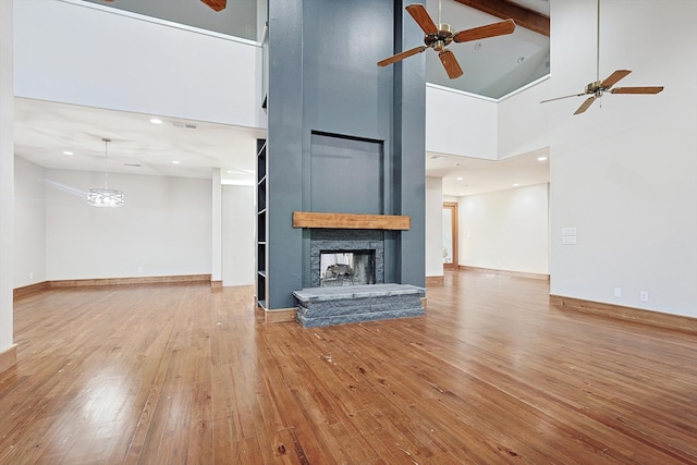 unfurnished living room featuring a fireplace, beam ceiling, high vaulted ceiling, light hardwood / wood-style floors, and ceiling fan