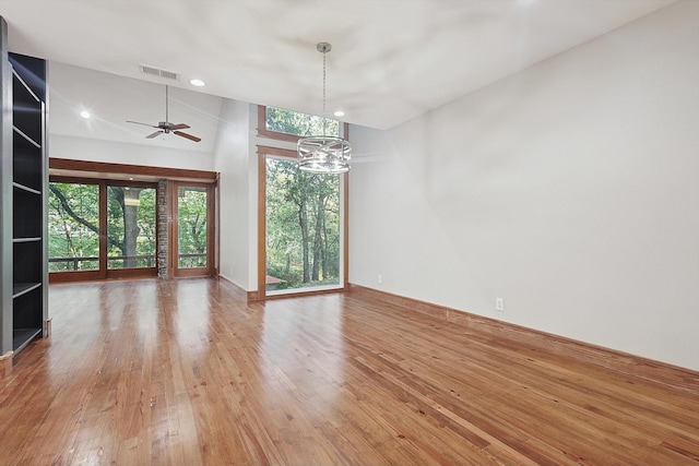 empty room with hardwood / wood-style floors, ceiling fan with notable chandelier, and a high ceiling