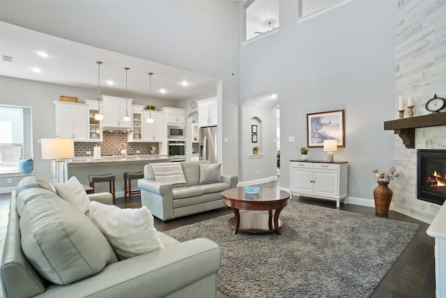 living room with dark wood-type flooring, sink, a towering ceiling, and a fireplace