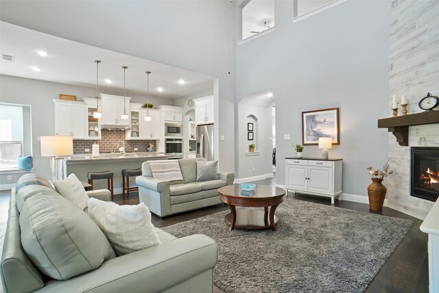 living room with dark wood-type flooring, sink, a towering ceiling, and a fireplace