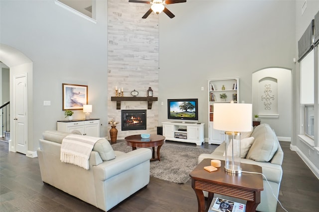 living room featuring a high ceiling, dark wood-type flooring, a tiled fireplace, and ceiling fan