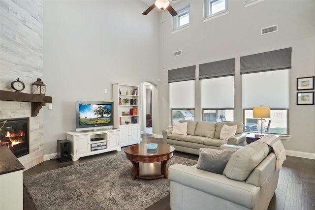 living room with a tiled fireplace, dark hardwood / wood-style flooring, ceiling fan, and a high ceiling