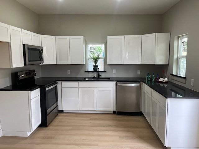 kitchen featuring white cabinets, dark countertops, appliances with stainless steel finishes, light wood-style floors, and a sink