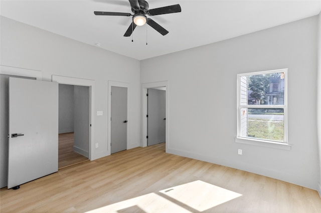 unfurnished bedroom featuring two closets, baseboards, a ceiling fan, and wood finished floors