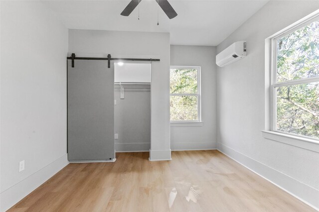 unfurnished bedroom featuring a barn door, baseboards, a ceiling fan, wood finished floors, and a wall mounted air conditioner