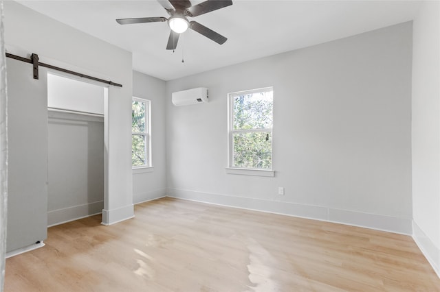 unfurnished bedroom featuring light wood-style floors, a wall unit AC, baseboards, and a barn door