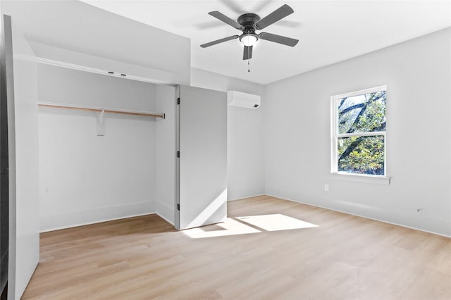 unfurnished bedroom with a closet, a wall unit AC, light wood-style flooring, and baseboards