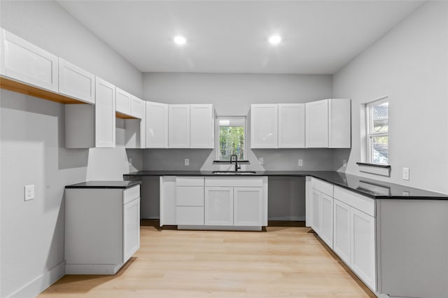 kitchen with light wood finished floors, dark countertops, white cabinetry, a sink, and recessed lighting