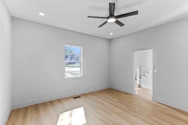 spare room featuring a ceiling fan, visible vents, baseboards, stairway, and light wood-type flooring