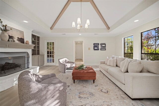 living room featuring wood-type flooring, a brick fireplace, a raised ceiling, and a notable chandelier