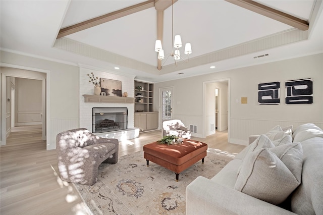 living room with built in shelves, an inviting chandelier, light hardwood / wood-style floors, a fireplace, and ornamental molding