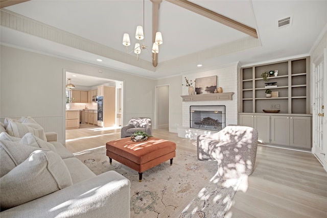 living room featuring a brick fireplace, a raised ceiling, light hardwood / wood-style flooring, a notable chandelier, and crown molding