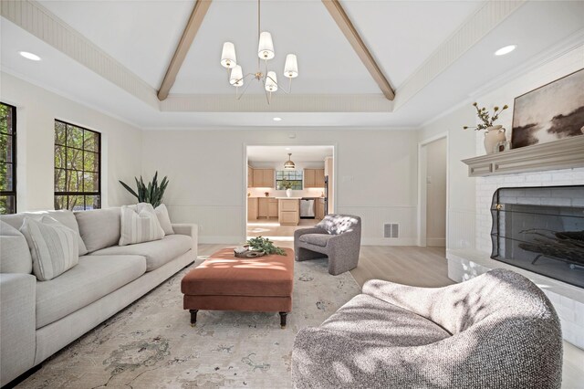 living room with vaulted ceiling with beams, light hardwood / wood-style floors, a brick fireplace, and ornamental molding