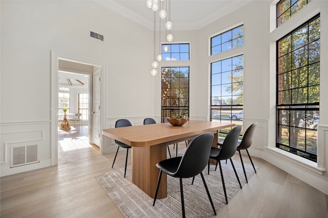 dining space featuring a towering ceiling, light hardwood / wood-style floors, and ornamental molding