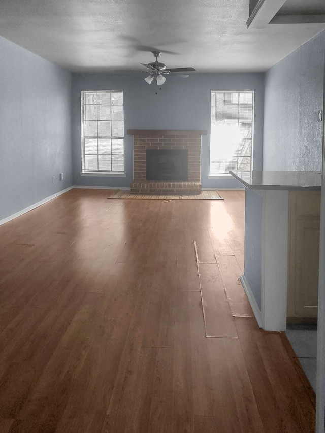 unfurnished living room featuring ceiling fan, a fireplace, a textured ceiling, and hardwood / wood-style flooring