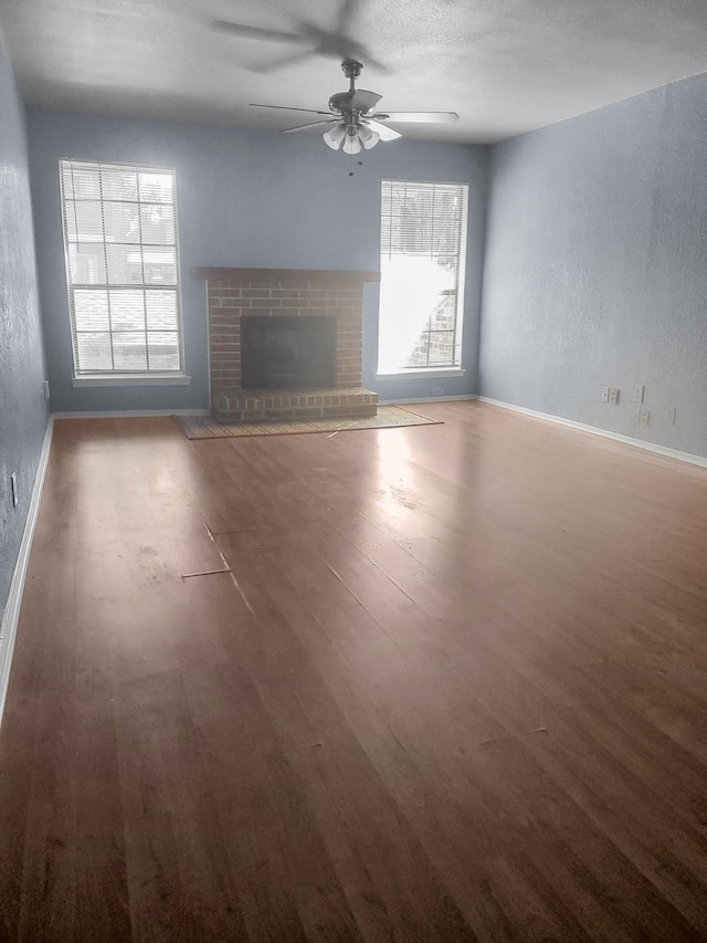 unfurnished living room with a textured ceiling, ceiling fan, dark wood-type flooring, and a brick fireplace