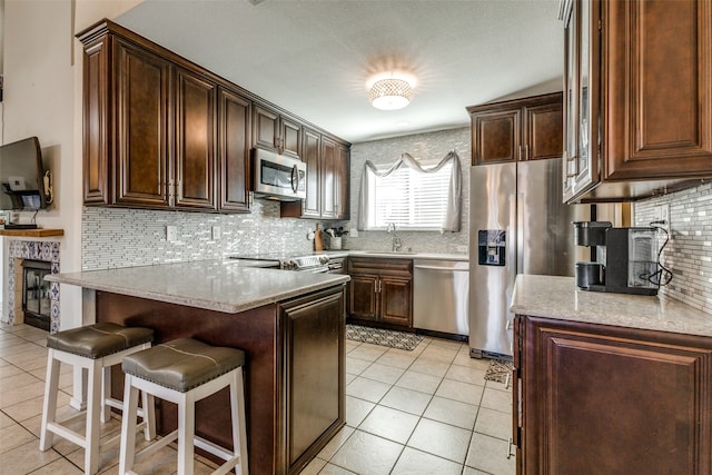 kitchen with appliances with stainless steel finishes, a kitchen breakfast bar, light stone countertops, light tile patterned floors, and decorative backsplash