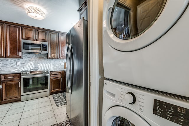 kitchen featuring stacked washer / dryer, appliances with stainless steel finishes, dark brown cabinets, light tile patterned floors, and light stone countertops