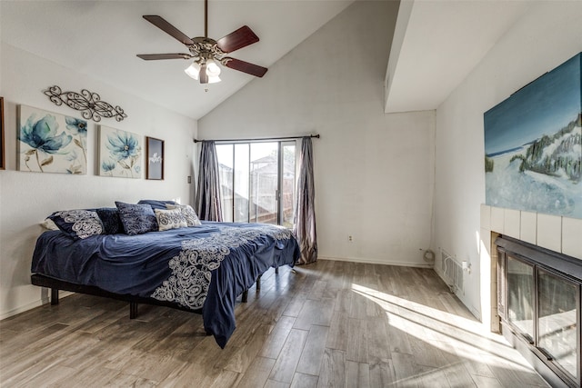 bedroom featuring high vaulted ceiling, a tile fireplace, ceiling fan, and light hardwood / wood-style flooring