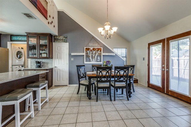 dining area featuring french doors, stacked washing maching and dryer, a notable chandelier, light tile patterned floors, and high vaulted ceiling