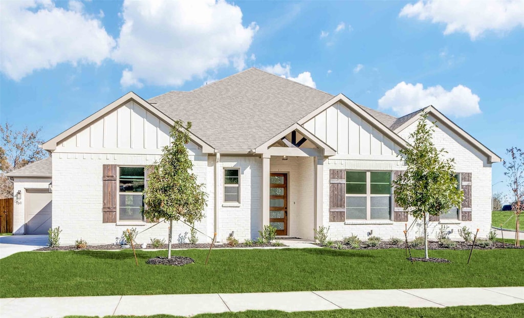 modern inspired farmhouse with roof with shingles, a front yard, board and batten siding, and brick siding