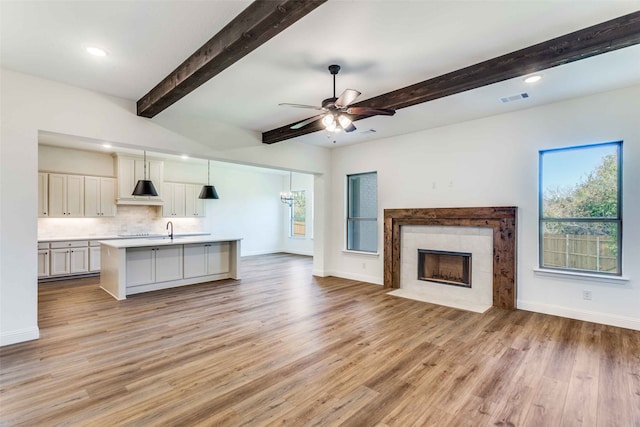 unfurnished living room featuring beamed ceiling, sink, ceiling fan, a fireplace, and light wood-type flooring