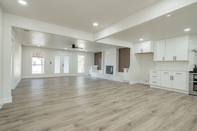 unfurnished living room with ceiling fan, light hardwood / wood-style flooring, a high end fireplace, and beamed ceiling