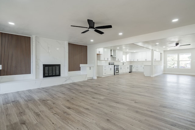 unfurnished living room with ceiling fan, light wood-type flooring, and a fireplace