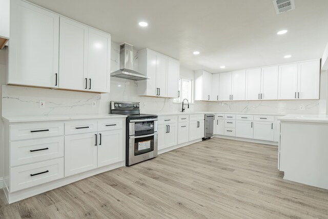 kitchen with appliances with stainless steel finishes, wall chimney exhaust hood, sink, light hardwood / wood-style flooring, and white cabinets