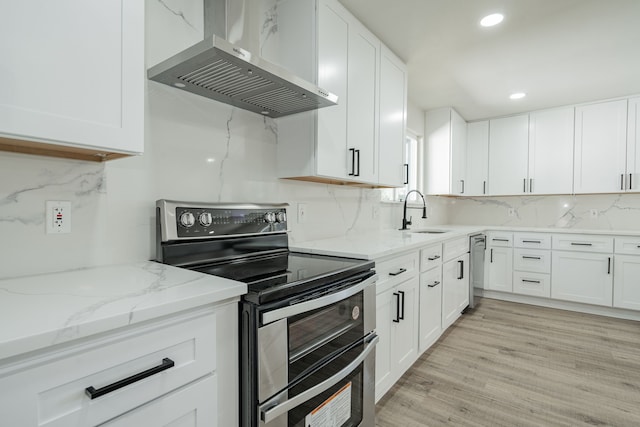 kitchen with appliances with stainless steel finishes, sink, wall chimney range hood, light hardwood / wood-style floors, and white cabinetry