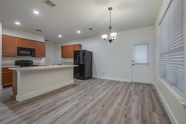 kitchen with light hardwood / wood-style floors, black appliances, a kitchen island with sink, pendant lighting, and sink