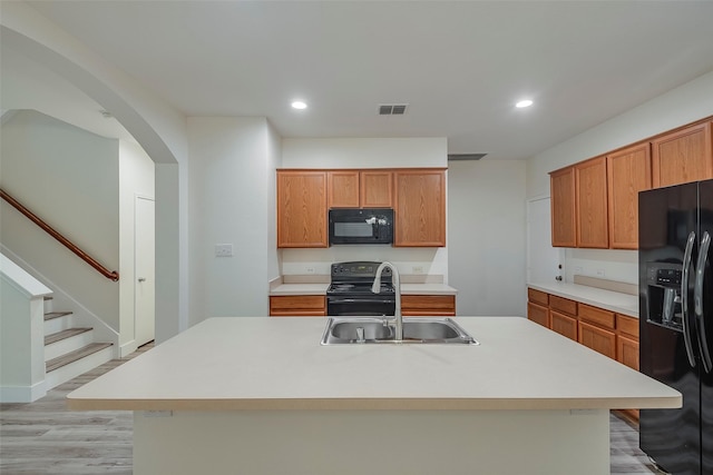 kitchen with black appliances, light hardwood / wood-style flooring, sink, and a center island with sink