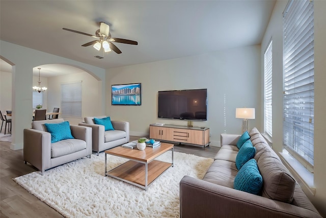 living area with baseboards, visible vents, arched walkways, wood finished floors, and ceiling fan with notable chandelier