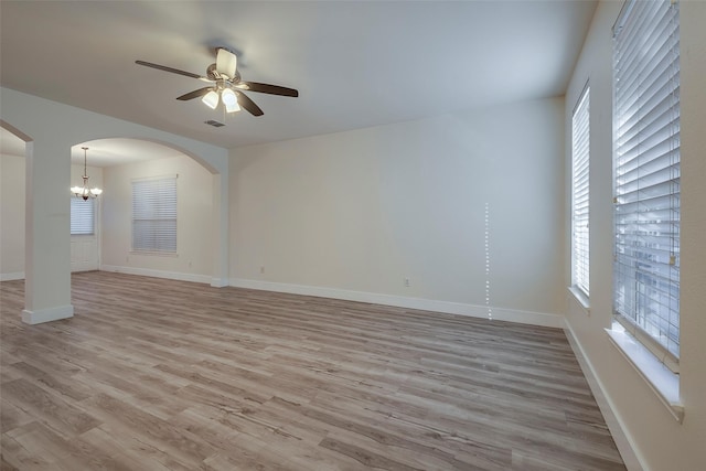 spare room featuring visible vents, arched walkways, baseboards, light wood-style flooring, and ceiling fan with notable chandelier