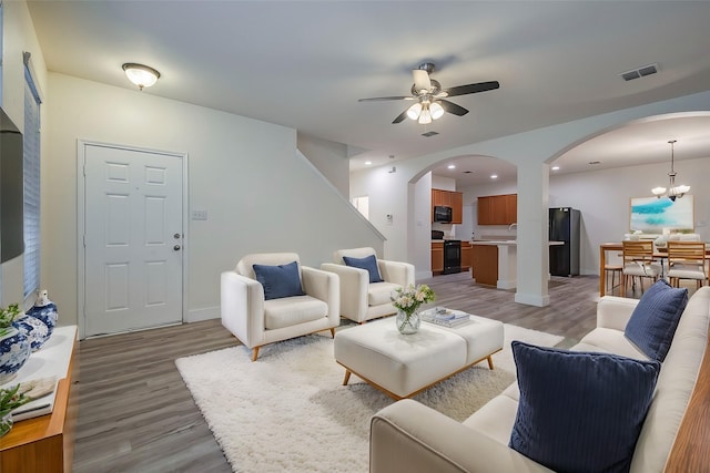 living area with arched walkways, recessed lighting, visible vents, light wood-type flooring, and ceiling fan with notable chandelier