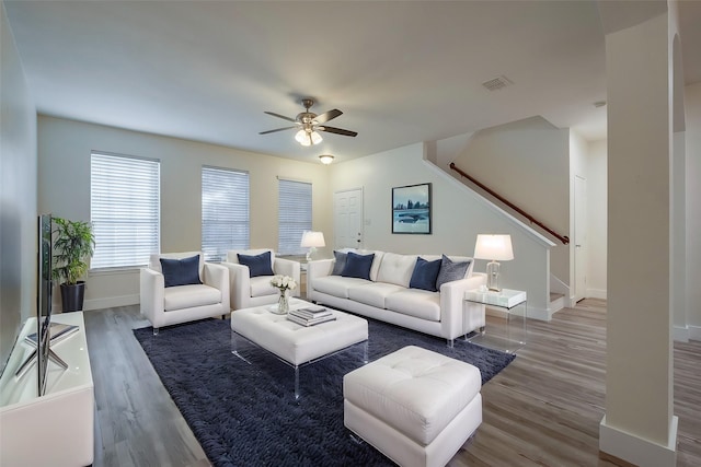 living room featuring baseboards, visible vents, ceiling fan, stairway, and wood finished floors